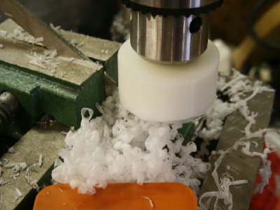 The piston is cut down to size and made round by raising and lowering it past a cutting tool.  Here a common wood chisel in the drill press vise works well.